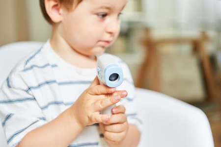 Child holds an infrared forehead thermometer for contactless measurement of a feverの写真素材