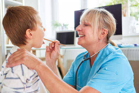 Pediatrician examines child with tonsillitis or sore throat with spatulaの写真素材