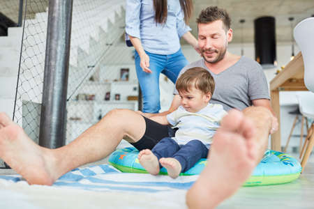 Father and son sit together in a rubber dinghy as toys in the living roomの写真素材