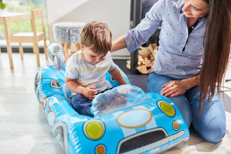 Child drives in the inflatable racing car with mother as supervision in the nurseryの写真素材