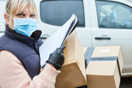 Parcel delivery woman with face mask checks delivery on list outside in front of her van