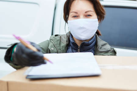 Delivery service parcel carrier with face mask asks for acceptance confirmation by signature
