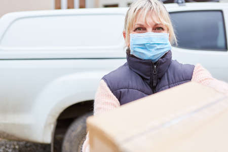 Parcel messenger with face mask outside in front of her vehicle delivers parcelの写真素材