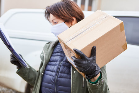 Delivery service parcel handler with face mask checks package delivery with list outsideの写真素材