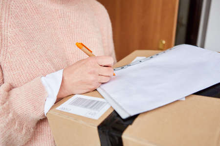 Woman gives a signature for a package in front of the apartment or house door delivery service