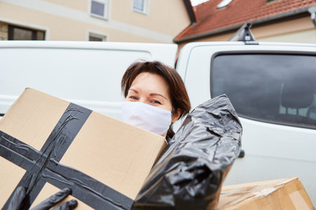 Delivery service parcel carrier with face mask outside carries out many parcels for deliveryの写真素材