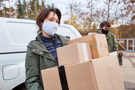Woman with face mask because of Covid-19 as a parcel carrier with parcels as delivery for Christmasの写真素材