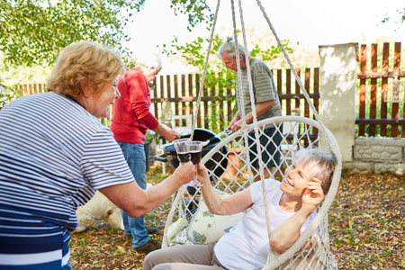 Seniors toast with a glass of red wine at the barbecue party in the garden in summerの写真素材