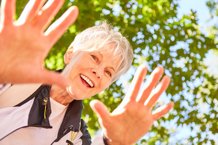 Laughing elderly woman waving her hands on a nature hike in summerの写真素材