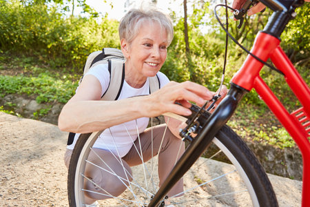 Senior woman doing DIY repair of bicycle or scooter after a breakdownの写真素材