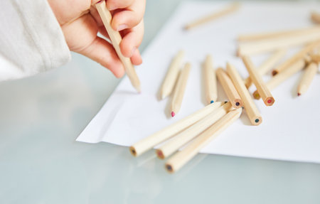 Little child is holding colored pencil while painting on a piece of paperの写真素材