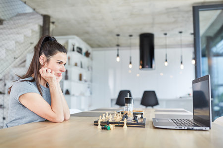 Woman at laptop is thinking about a problem playing chess in video chat onlineの写真素材