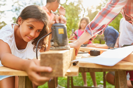 Children grinding wood in teamwork in the craftsman workshop at the holiday campの写真素材