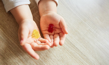 Child holds a gummy bear in each hand as a candy to choose fromの写真素材