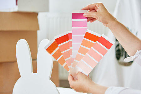 Hands of woman hold paint fan while painting chair during house renovationの写真素材