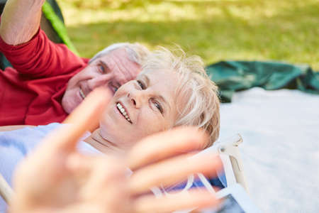 Happy senior retired couple cheerfully lies in front of the tent in nature in summerの写真素材