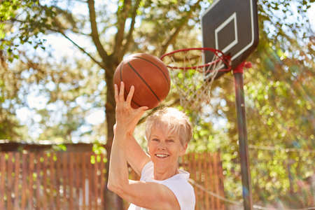 Sporty elderly woman playing basketball for fitness and health in summerの写真素材