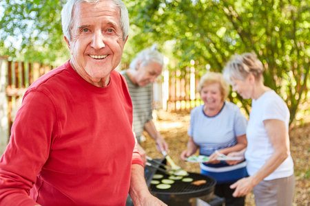 Smiling senior retirees with friends having a barbecue together in the gardenの写真素材