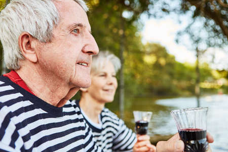 Happy senior couple drinking wine in nature by the lake on weekend