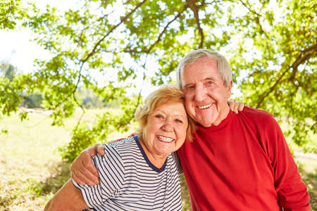 Happy senior pensioner couple in love standing arm in arm in the park in summer