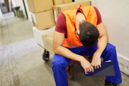 Exhausted worker in the warehouse with packages takes a break due to overloadの写真素材