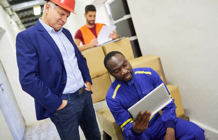 Boss and warehouse clerk at the tablet computer with packages before shipping in online retail