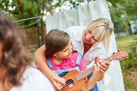 Girl practices playing guitar with the help of teacher in guitar class at summer camp
