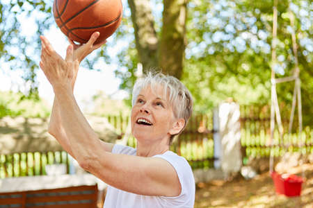 Senior woman as a sporty and energetic pensioner playing basketball in summerの写真素材
