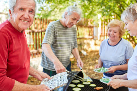 Seniors as friends or retirees have a barbecue together at a garden party in summerの写真素材