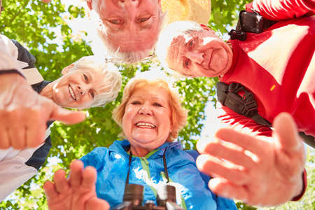 Group of active seniors in a hiking group in nature in summer beckoning happily