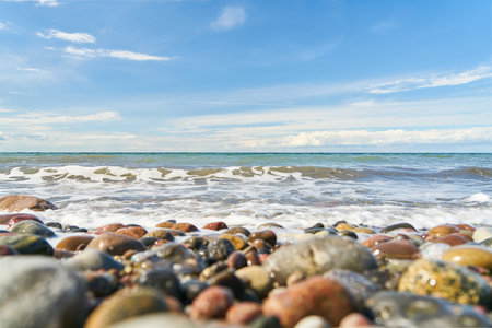 Pebbles on the beach by the sea with waves and sky with cloudsの写真素材