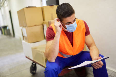 Warehouse clerk with face mask because of Covid-19 with a checklist at the incoming goods departmentの写真素材