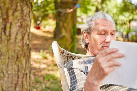 Smiling senior retired man reading book while relaxing in gardenの写真素材