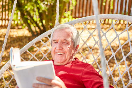 Retired happy senior man reading book in garden in summerの写真素材