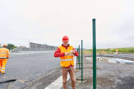 Construction worker with guideline at the fence construction on the road construction site