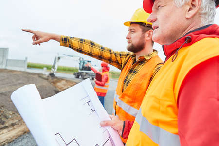 Architect and site manager with floor plan on the construction site of building a house with excavatorの写真素材