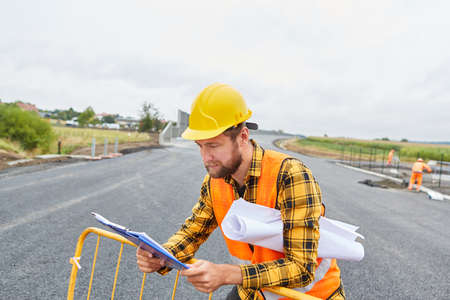 Worker on the construction site of road construction with checklist and site plan for building developmentの写真素材