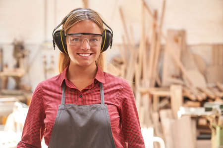 Woman as a carpenter apprentice with safety glasses and hearing protection in the carpentry workshopの写真素材
