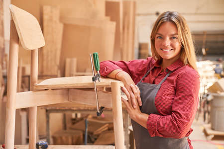 Young woman as a carpenter apprentice gluing chair in the cabinet makingの写真素材