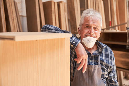 Senior craftsman as master with face mask because of Covid-19 in the joinery
