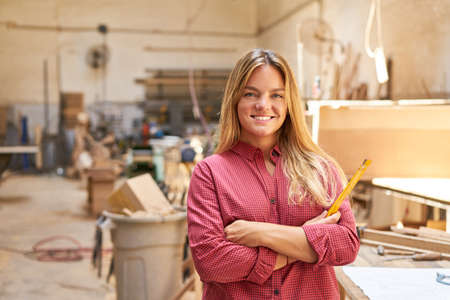 Young woman as a craftsman trainee in the carpenter apprenticeship in the carpentry workshopの写真素材