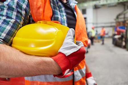 Worker or craftsman with hard hat and gloves in a factory hallの写真素材