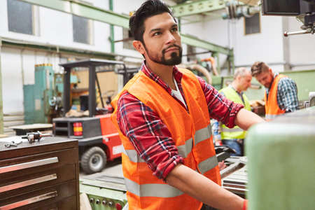 Metal worker in the production of the metal factory operates a machine using a large wheel