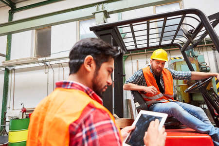 Forklift driver and warehouse worker with tablet computer in the shipping company or metal factory