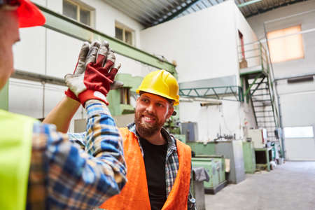 Two workers greet each other with high five in the metalworking factoryの写真素材