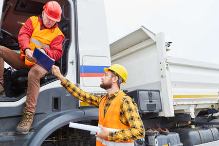 Construction manager with checklist and truck driver discuss delivery at the construction site