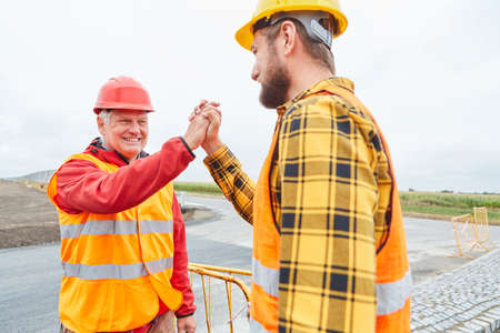 Two road construction workers celebrate success with handshake