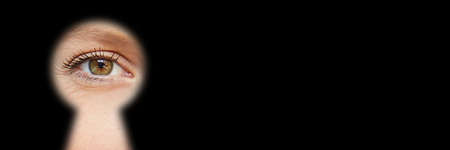 Woman looks through a blurred keyhole as a spy or detective with copy spaceの写真素材