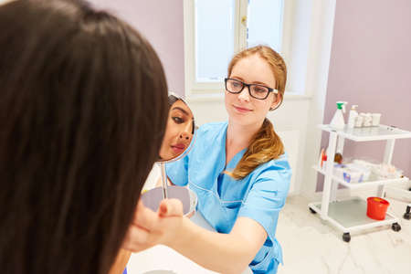 Woman and beautician with mirror in consultation before cosmetic surgeryの写真素材