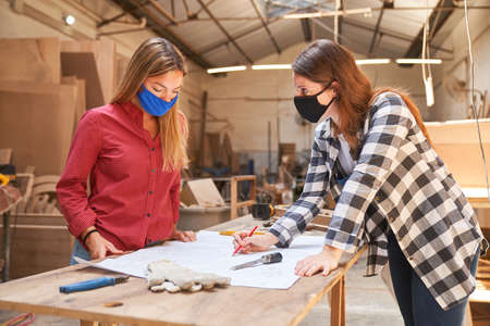 Two craftsmen women with face masks because of Covid-19 in front of a construction planの写真素材